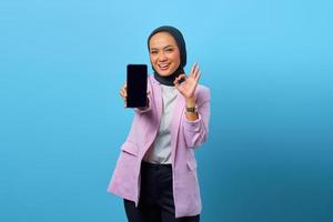 Mujer asiática que muestra la pantalla en blanco del teléfono inteligente y gesticula el signo bien