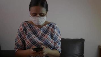 Woman wears face mask chatting and using data tracking on smartphone video