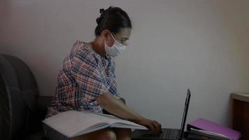 mulher usa máscara facial trabalhando com laptop e documento na sala de estar