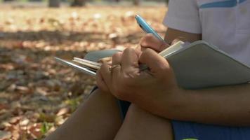 femme assise sous un arbre et écrivant sur un journal en été