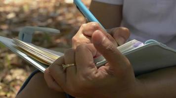 Close up woman's hands écrit pour planifier le travail sur le journal sous un arbre video