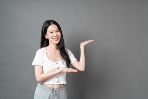 Mujer asiática con rostro sonriente y presentación de la mano en el lateral foto