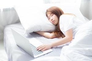 hermoso de retrato joven mujer asiática con laptop acostada en el dormitorio, niña cansada de dormir y relajarse con computadora portátil, descanso y concepto de salud. foto
