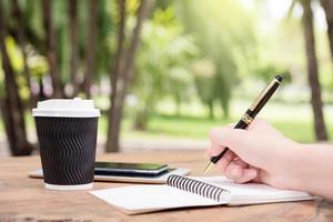 La mano de la mujer toma notas con un bolígrafo en un cuaderno y toma café foto