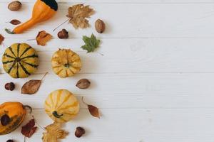 Pumpkins, dried leaves on white wooden background top view. Autumn. photo