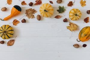 Pumpkins, dried leaves on white wooden background top view. Autumn. photo