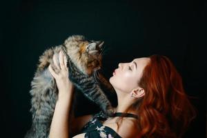 Red-haired woman hugs fluffy cat on black background