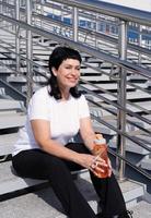 Senior woman drinking water after workout outdoors on urban background photo