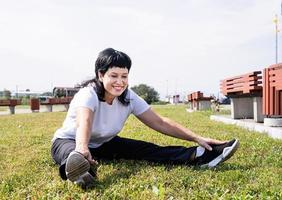 Mujer calentando estiramientos sentados en el césped del parque foto