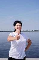 Mujer en ropa deportiva mostrando los pulgares para arriba trabajando cerca de la orilla del río foto