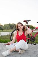 Teenage girl sitting next to her bike in the park listening to music photo