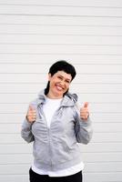 Woman showing thumbs up standing outdoors on gray solid background photo