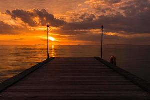 Puente de madera al mar con puesta de sol.