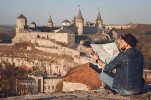 Traveler man with a map in his hands sits on background of old castle photo