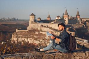Traveler man with a map in his hands sits on background of old castle photo