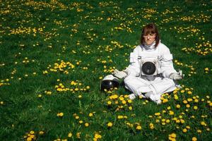Mujer astronauta sin casco se sienta en un césped verde entre flores foto