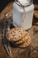Cereal cookies with a jug of milk on a wooden background.