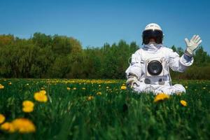 Astronauta futurista en un casco se sienta en un césped verde entre flores
