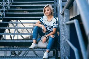 woman with short white hair in urban style sits on the metal stairs