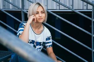 woman with short white hair in urban style sits on the metal stairs photo