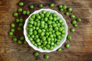 Fresh green peas in a white plate on wooden background photo