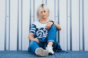 Mujer con pelo corto y blanco se sienta en el fondo de la pared de metal foto