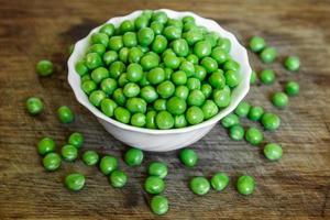 Fresh green peas in a white plate on wooden background, top view photo