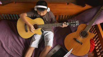 garçon apprend à jouer de la guitare en ligne à la maison