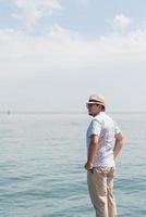 Hombre con sombrero de pie en el muelle con el mar de fondo foto