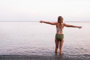 young woman standing on stony beach with outstretched arms