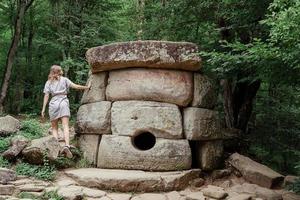 Woman in summer dress walking near big dolmen stone in the forest photo