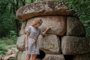 Mujer en vestido de verano caminando cerca de la gran piedra dolmen en el bosque