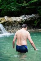 Hombre nadando en el río de la montaña con una cascada. foto