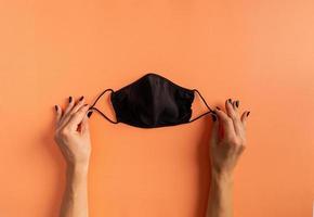 Woman hand with black nails holding black protective mask photo