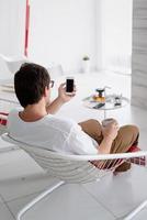 Man sitting in a chair watching tv holding tea cup and phone photo