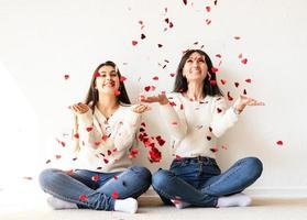 Two best friends having fun at home blowing red confetti photo