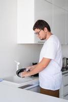 Hombre de camiseta blanca lavando platos en la cocina foto