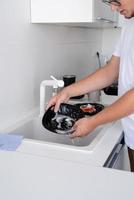 Hombre de camiseta blanca lavando platos en la cocina foto