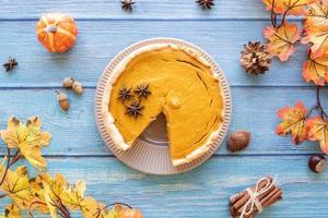 Homemade pumpkin pie with autumn leaves on rustic background, top view photo