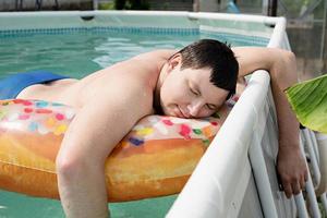 Young man sleeping on inflatable swim ring in the pool photo