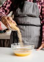 Joven mujer latina vertiendo azúcar en la masa para cocinar en la cocina foto