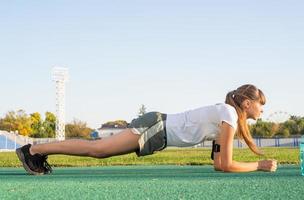 Teenager girl in a plank position doing workout at the stadium photo