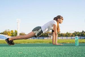 Teenager girl workout standing in a plank position at the stadium photo