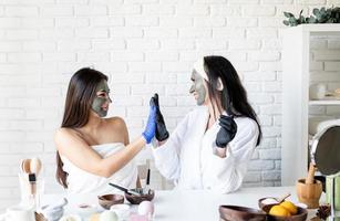 Two beautiful women in gloves applying facial mask having fun photo