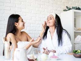 Two beautiful women applying facial cream doing spa procedures photo