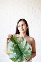 mujer sosteniendo una hoja de monstera verde delante de su cara foto