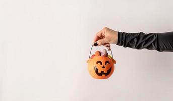 Woman's hand with black nails holding pumpkin full of sweets on white background