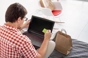 Back view of man shopping on internet with laptop looking photo