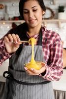 Mujer latina vertiendo la miel en la masa que se cocina en la cocina foto