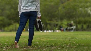 Mujer caminando descalza en el parque, sosteniendo sus zapatos deportivos foto